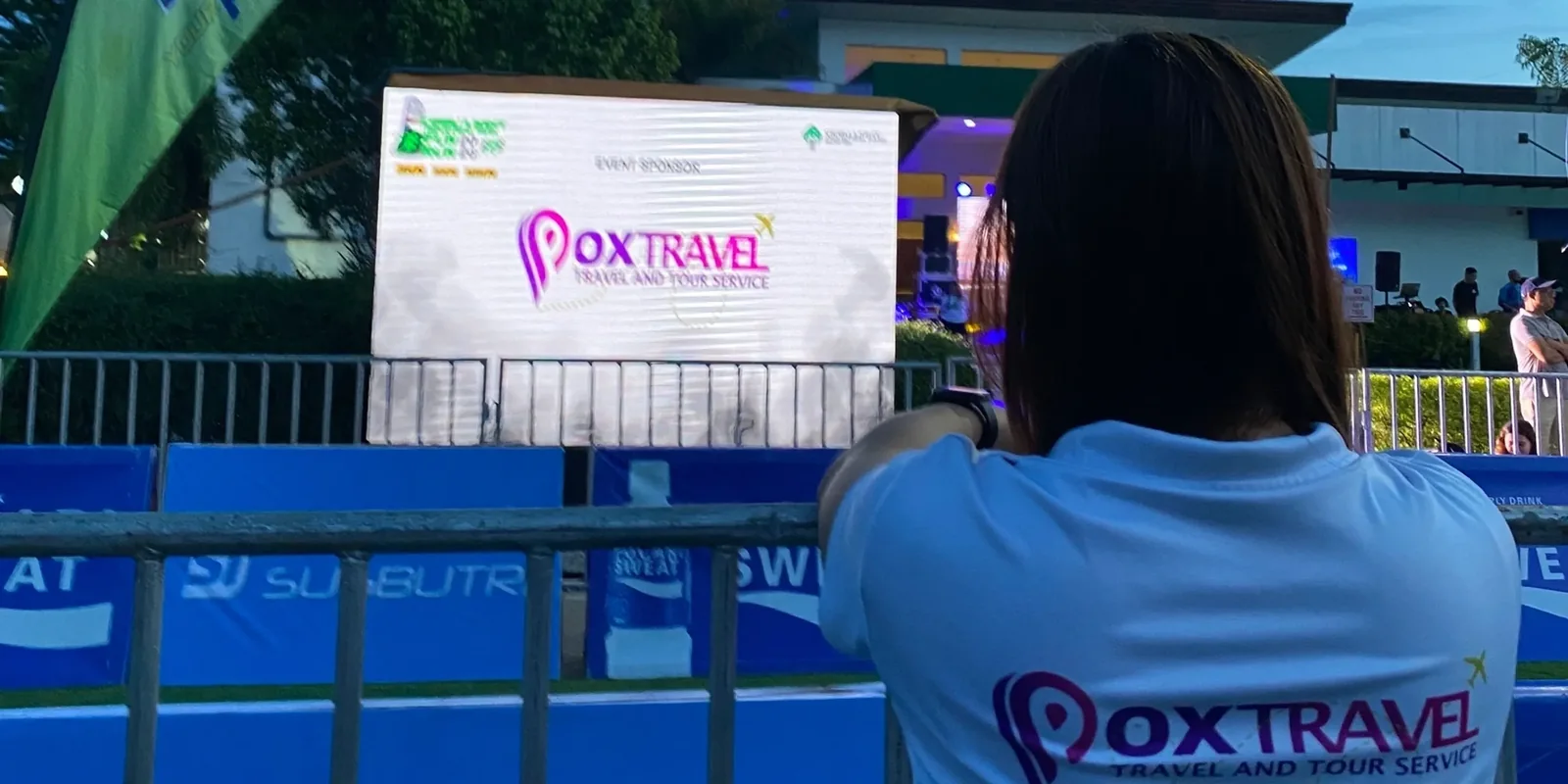 Pox Travel team member at the Cebu Light Industrial Park 2026 Fun Run, with the Pox Travel event sponsor screen