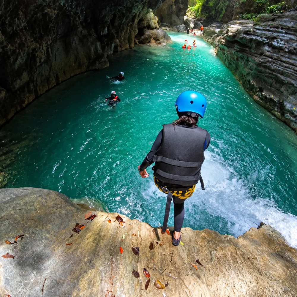 A canyoneer in a helmet and life vest about to jump into the turquoise river canyon in Badian